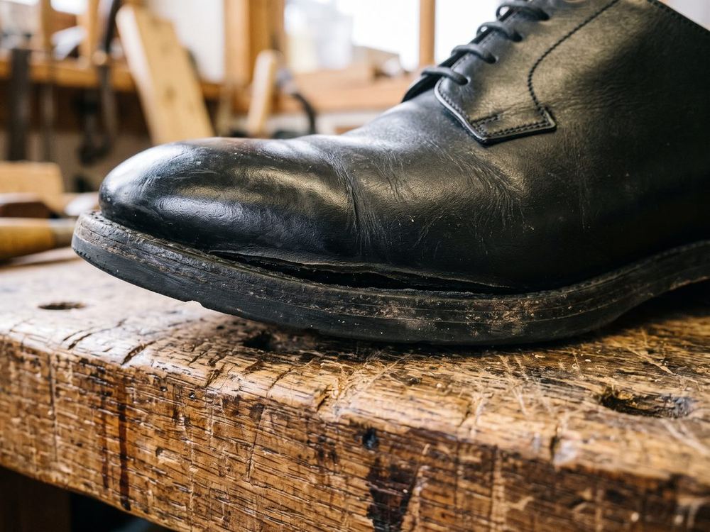 Close view of the edge of a black leather shoe. There is no stitching, only a glued seam, and the sole is lifting away from the upper near the toe.