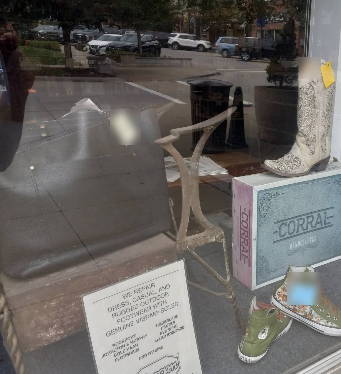 A second view into the Mace Shoe Repair window: a leather bench seat, a cast-iron shoe-stretching stand, a boot box, canvas high-tops, and the shop's printed repair card listing Rockport, Johnston & Murphy, Cole Haan, Florsheim, Timberland, Dexter, Red Wing and Allen Edmonds.